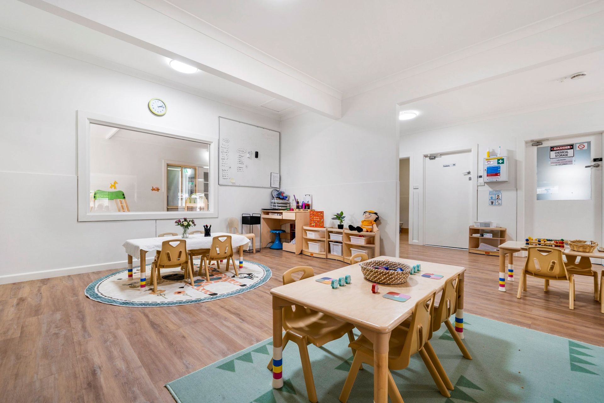 Preschool classroom with small tables, chairs, and educational toys on wooden floors.